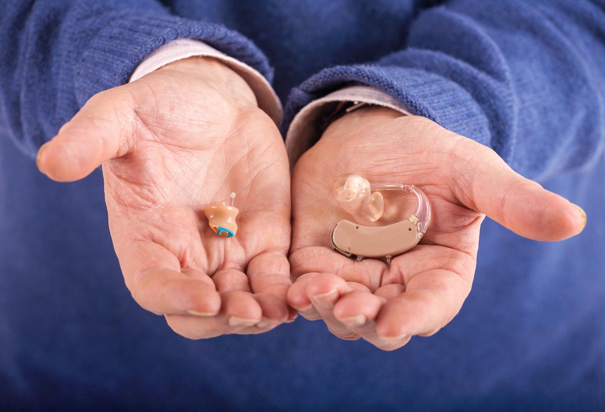 older gentleman cradling a CIC hearing aid in one hand and a BTE hearing aid in the other